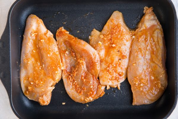 Raw marinated chicken breasts in a casserole dish