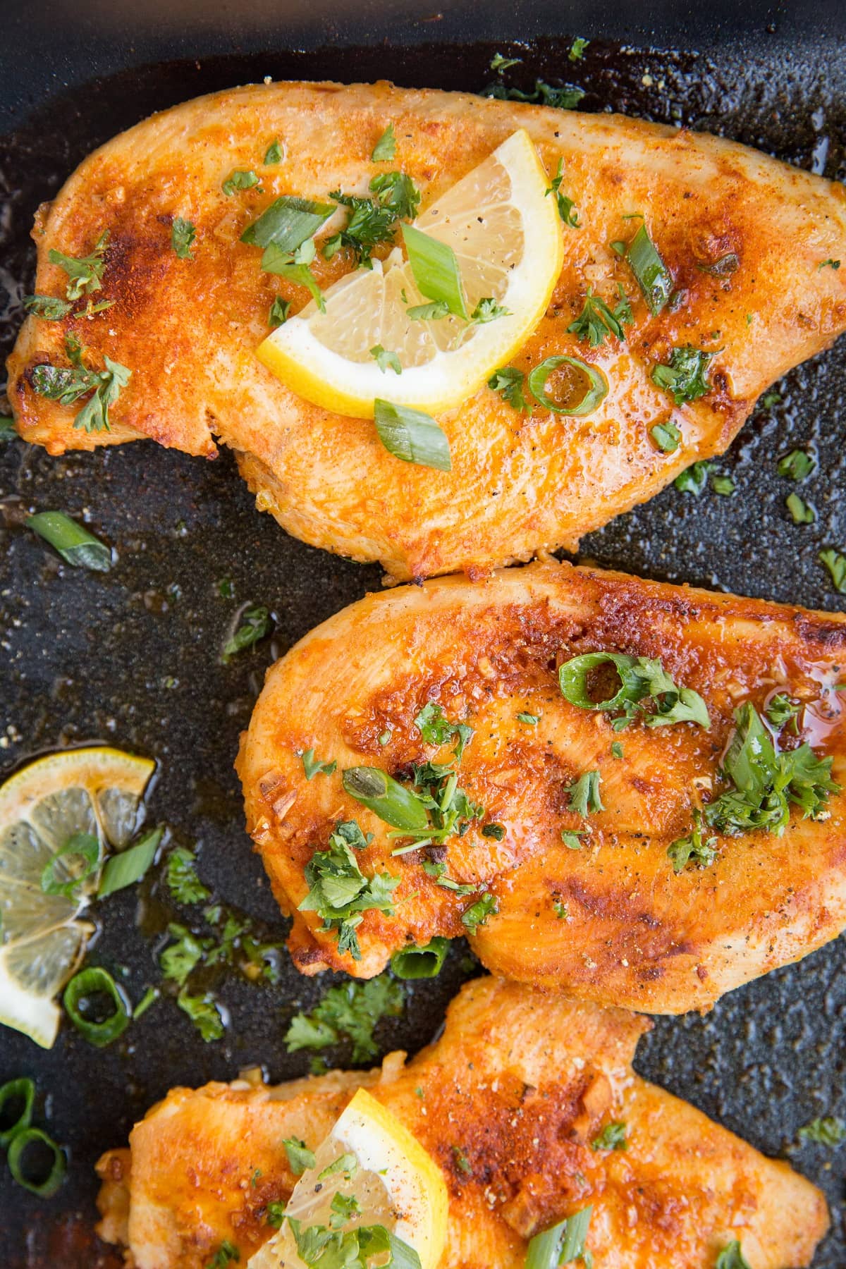 top down photo of baked chicken breasts in a casserole dish with slices of lemon on top and green onions