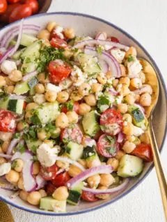 Angle shot of chickpea salad in a bowl with a gold spoon and a wooden bowl of tomatoes