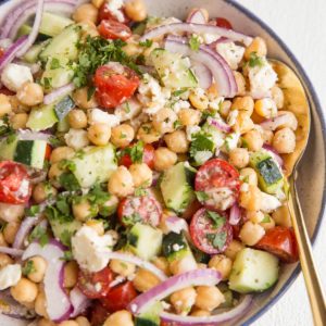Angle shot of chickpea salad in a bowl with a gold spoon and a wooden bowl of tomatoes