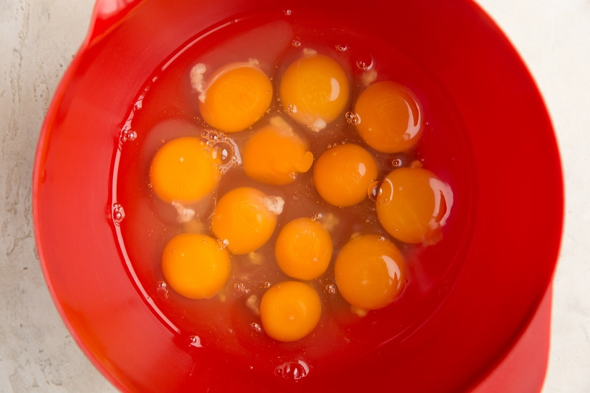 Twelve raw eggs in a mixing bowl, ready to be whisked