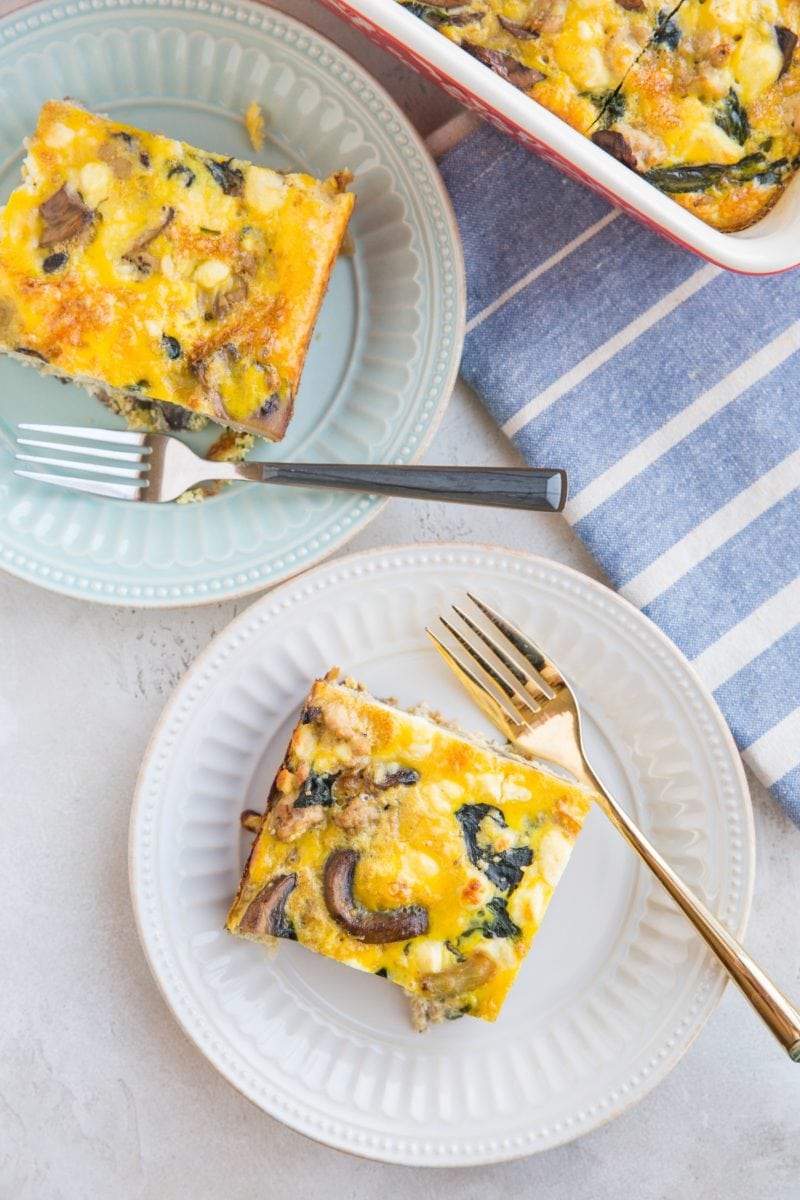 two plates with two slices of sausage and mushroom breakfast casserole with a blue striped napkin to the side.