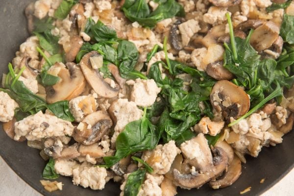 Baby spinach, sausage, mushrooms, onion and garlic cooking in a skillet