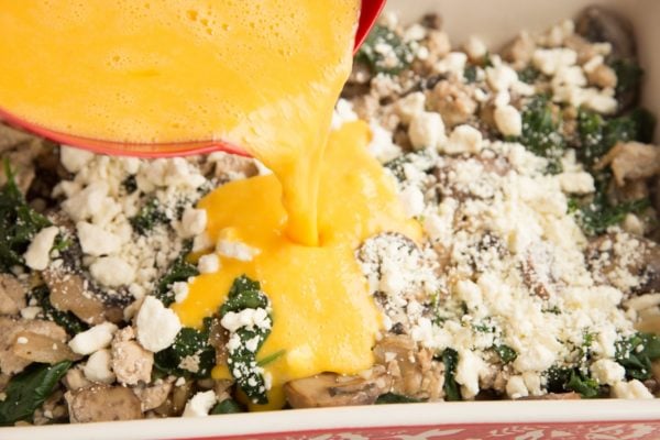 Beaten eggs being poured over the meat and vegetable mixture in the casserole dish.