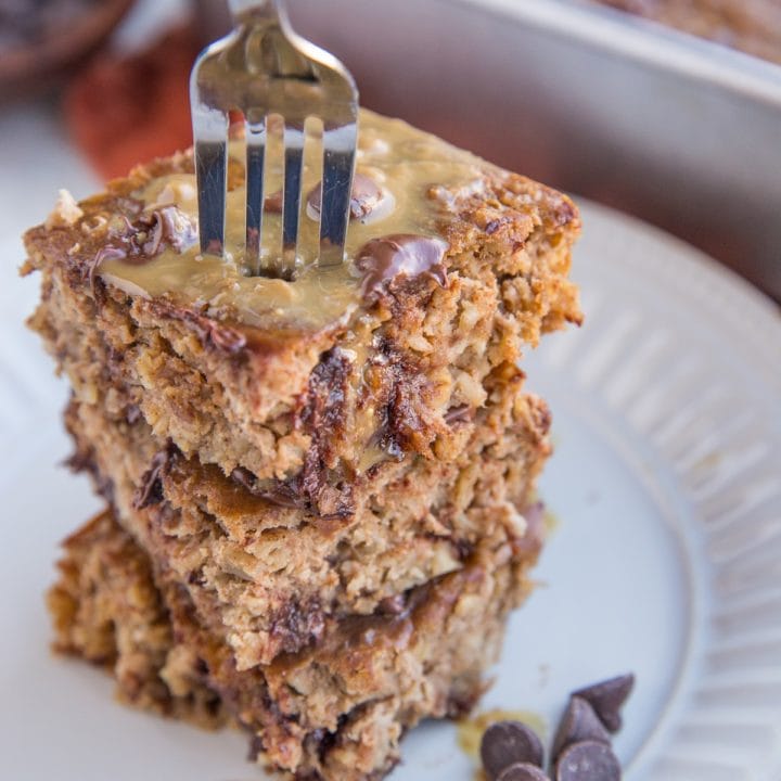 Stack of baked oatmeal on a white plate with a fork taking a bite out.
