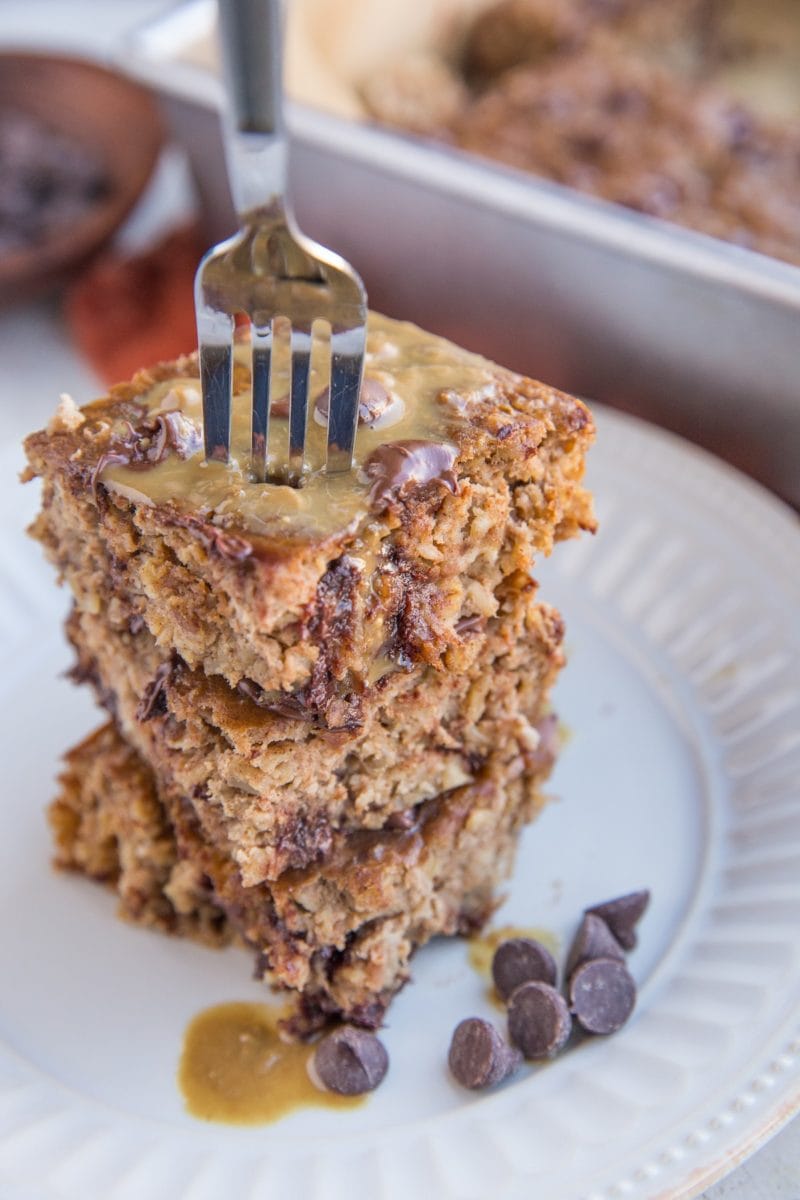Stack of baked oatmeal on a white plate with a fork taking a bite out.