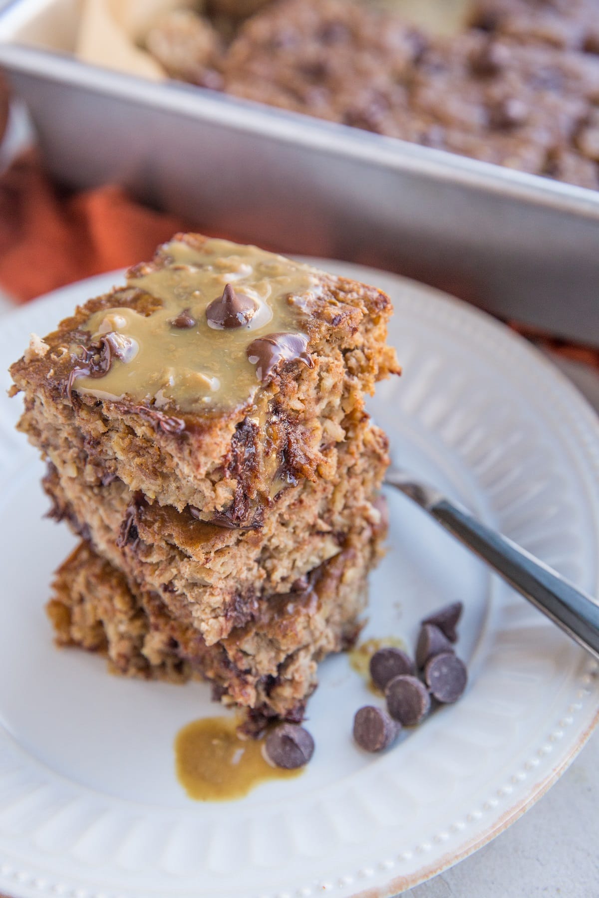 Banana Peanut Butter Baked Oatmeal stacked on a plate with the baking dish in the background