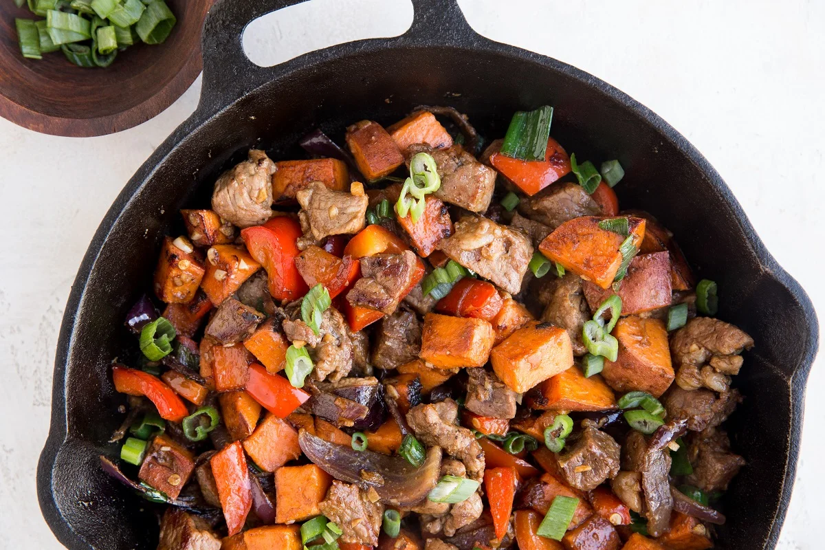 Cast iron skillet of beef tips, sweet potatoes, and bell pepper