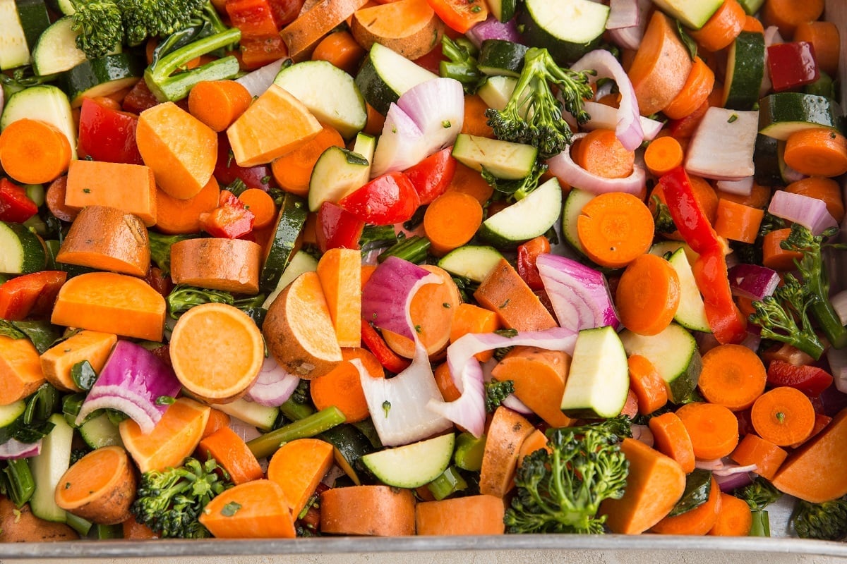 Raw vegetables seasoned with salt and oil in a large roasting pan, ready to go into the oven.