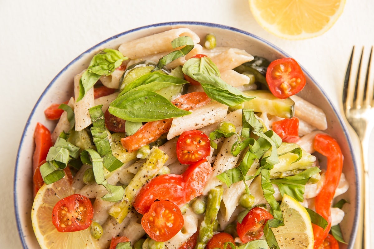 hortizontal top down photo of a big bowl of vegan pasta primavera with all sorts of fresh vegetables