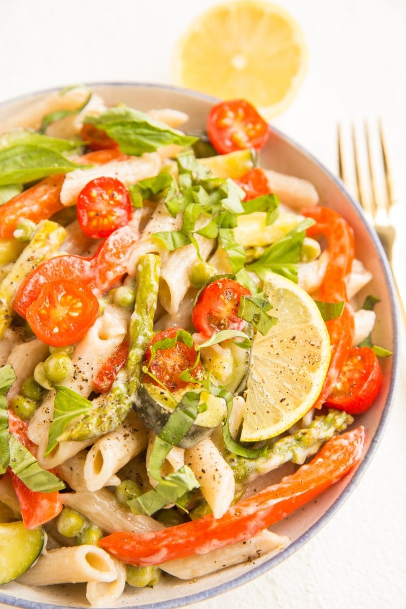 Close up image of vegan pasta primavera with a slice of lemon and fresh basil