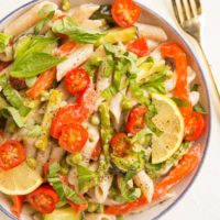 Top down photo of bowl of pasta primavera with a fork to the side and a lemon