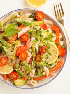 Top down photo of bowl of pasta primavera with a fork to the side and a lemon