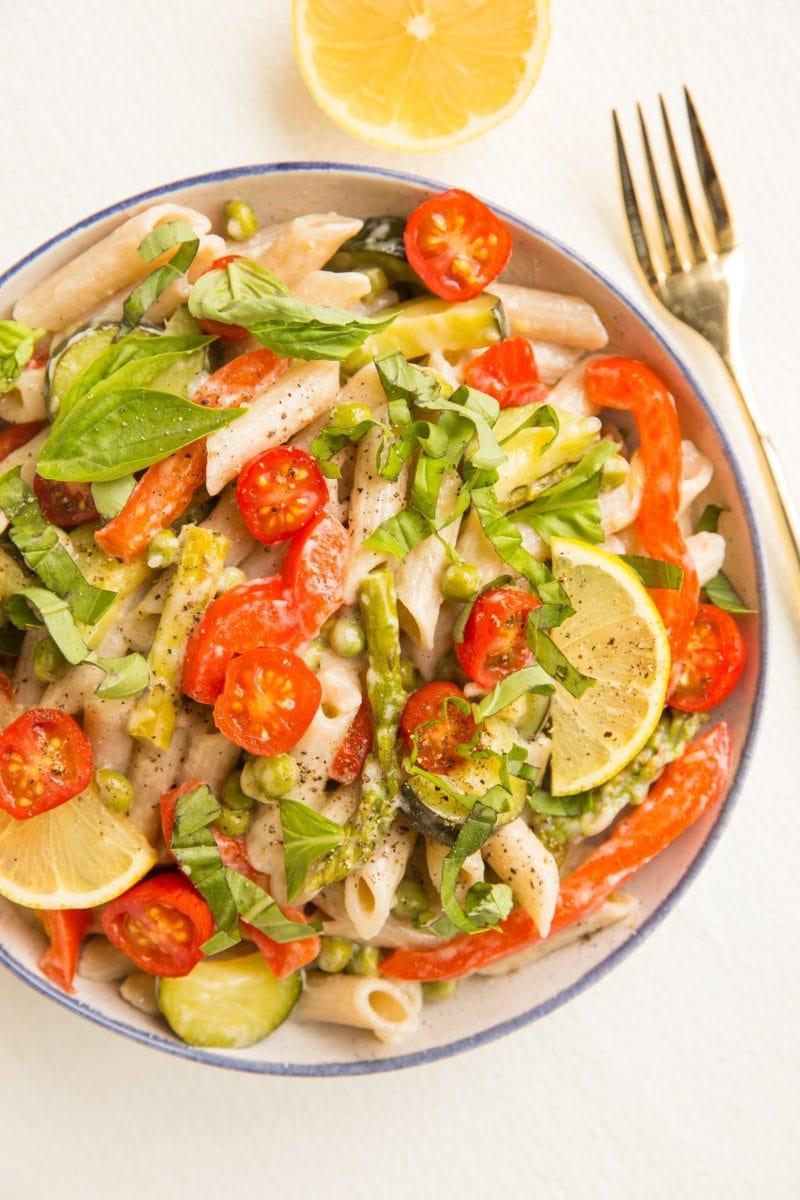 Top down photo of bowl of pasta primavera with a fork to the side and a lemon