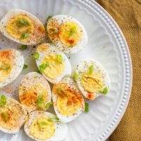 Hard boiled eggs sliced in half and sprinkled with salt, pepper, and paprika and green onions on a white plate