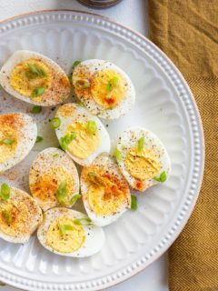 Hard boiled eggs sliced in half and sprinkled with salt, pepper, and paprika and green onions on a white plate