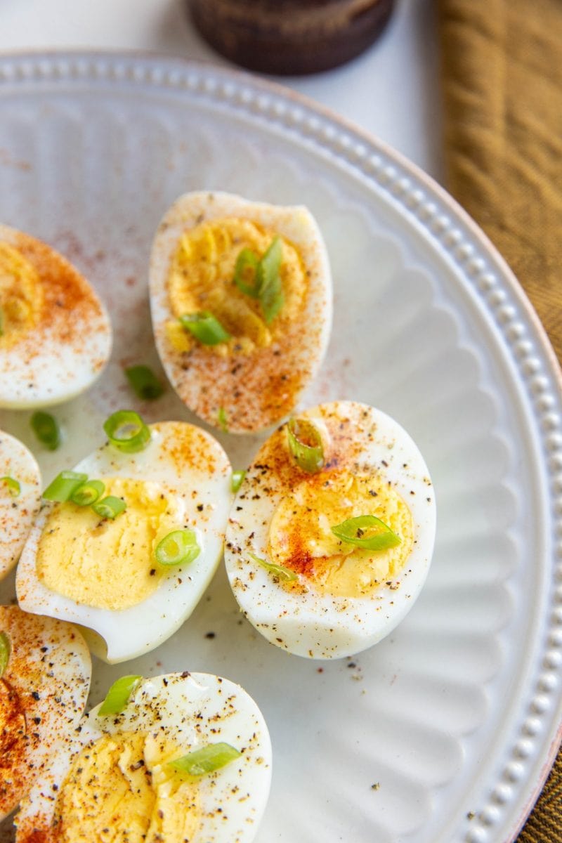 Hard boiled eggs sprinkled with paprika and chopped green onion on a white plate