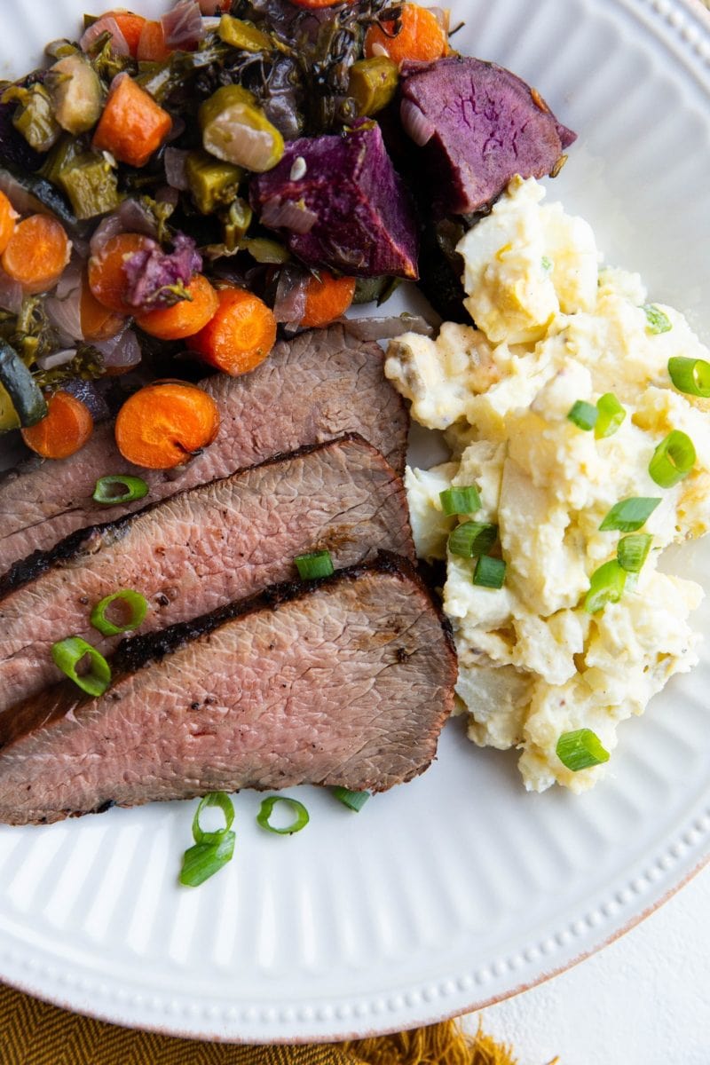 BBQ Tri tip on a plate with roasted vegetables and potato salad
