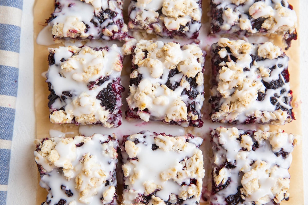 horizontal photo of blackberry crumb bars on parchment paper drizzled with glaze