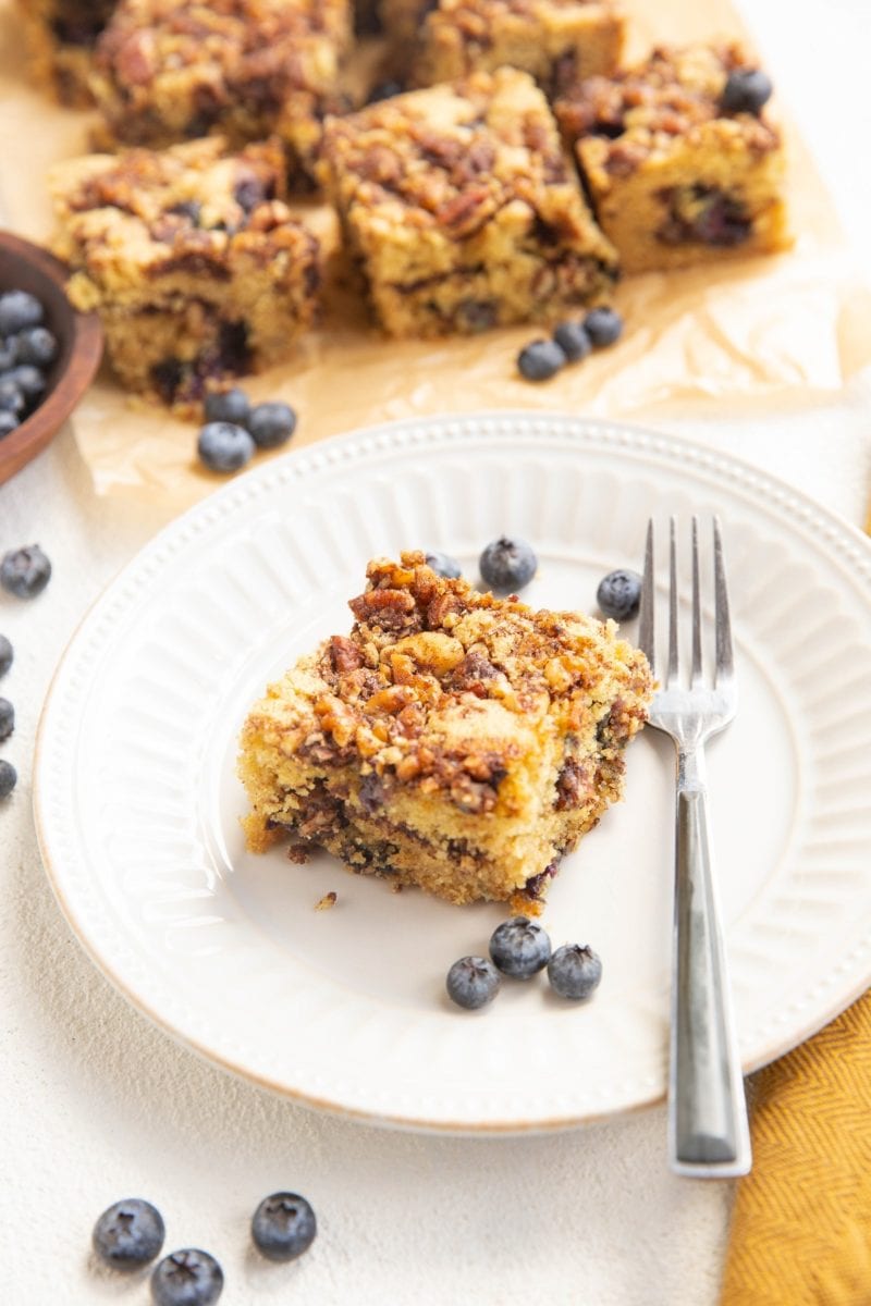 Slice of coffee cake on a plate with coffee cake in the background.