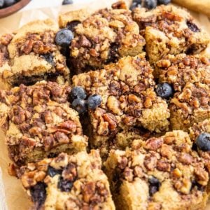 Slices of gluten-free coffee cake on a piece of parchment paper with blueberries to the side.