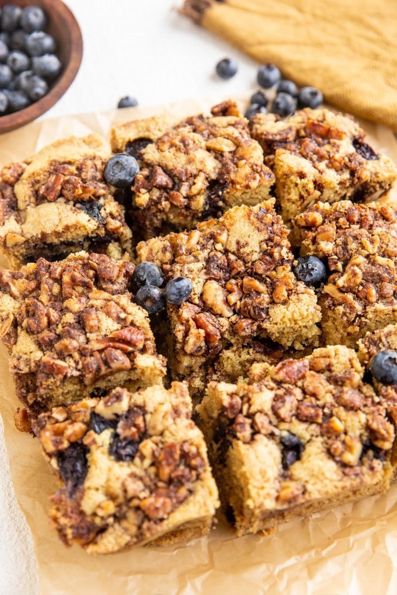 Slices of gluten-free coffee cake on a piece of parchment paper with blueberries to the side. 