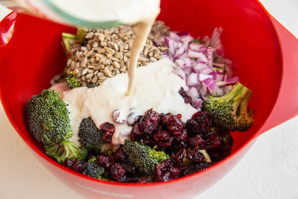 Pouring creamy dressing over broccoli salad