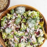 Wooden bowl full of broccoli salad with a striped napkin to the side and a bowl of sunflower seeds