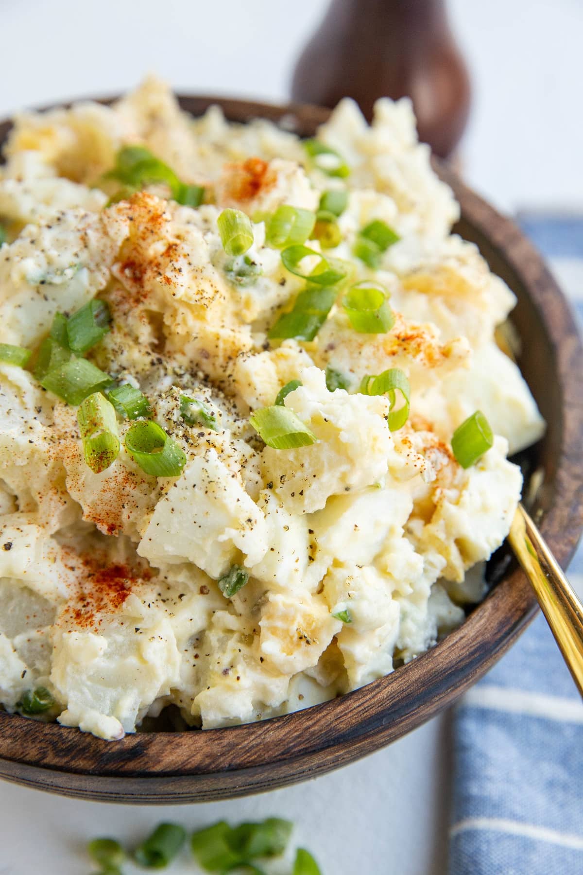 Large wooden bowl of potato salad with a blue striped napkin to the side and a golden spoon.