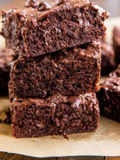 Stack of three coconut flour brownies with gooey chocolate shining through.