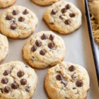 Coconut flour chocolate chip cookies on parchment paper on a baking sheet with a napkin to the side