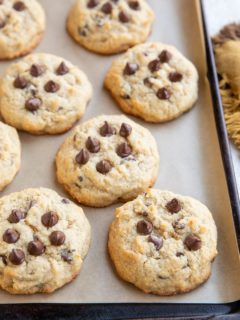 Coconut flour chocolate chip cookies on parchment paper on a baking sheet with a napkin to the side