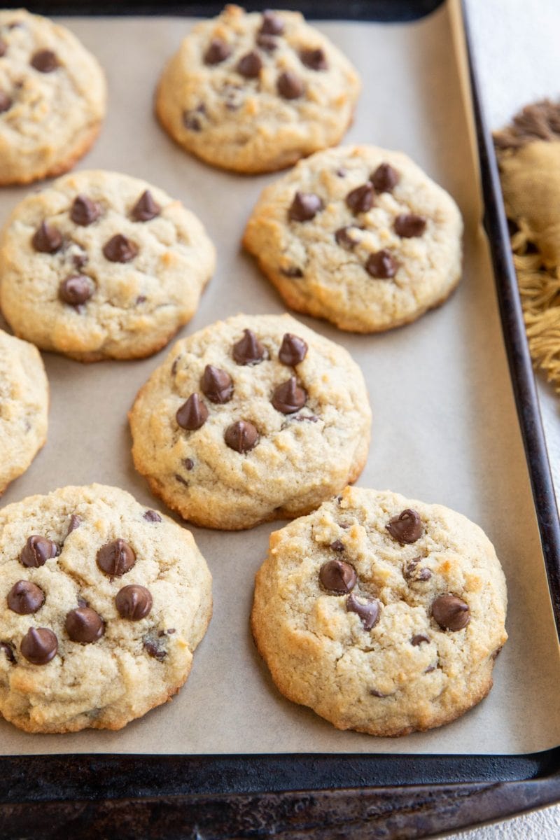 Coconut flour chocolate chip cookies on parchment paper on a baking sheet with a napkin to the side