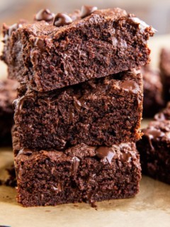 Stack of three coconut flour brownies with gooey chocolate shining through.
