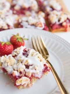 strawberry oatmeal bar on a plate with a gold fork and bars in the background
