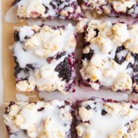 slices of blackberry crumb bars on parchment paper with glaze drizzled on top.