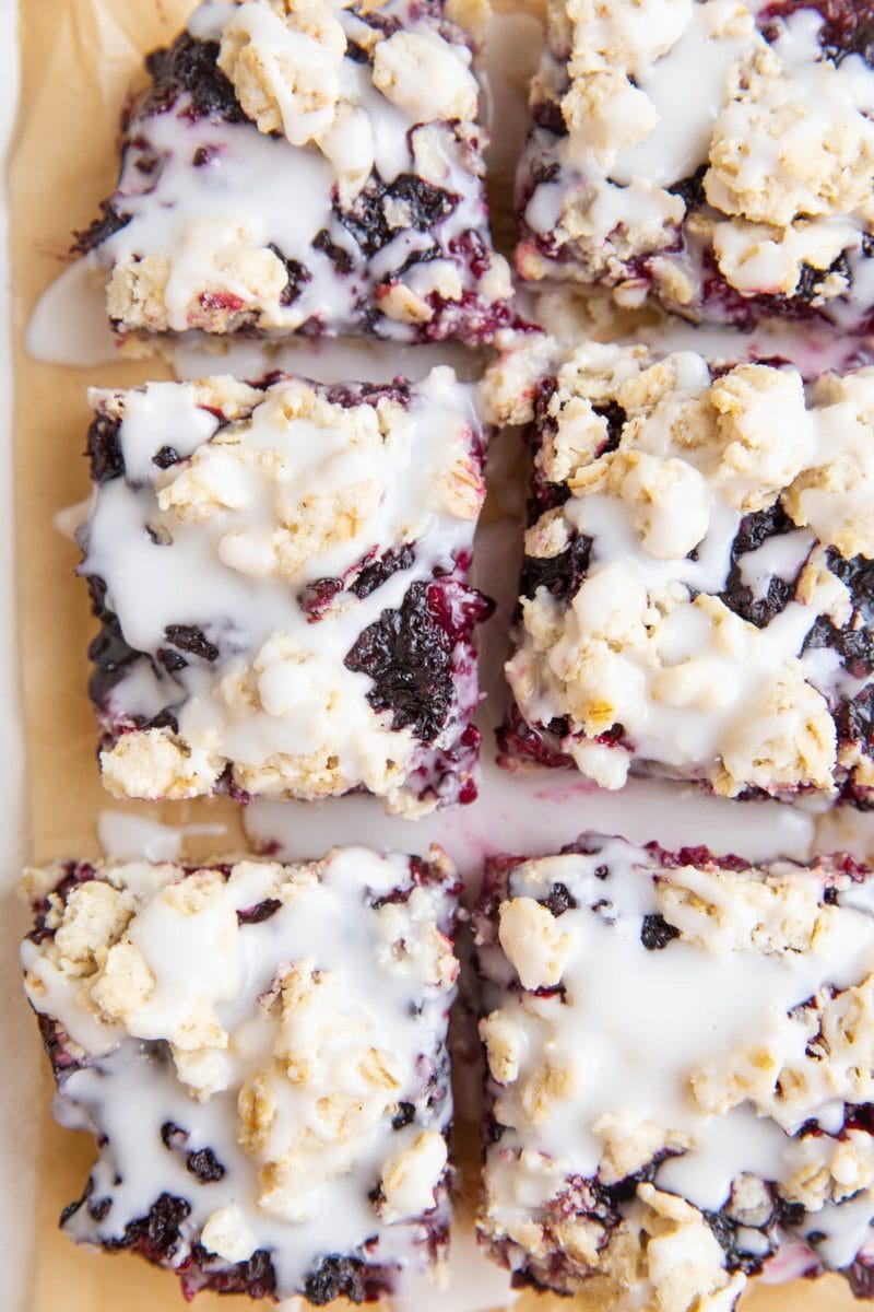 slices of blackberry crumb bars on parchment paper with glaze drizzled on top.