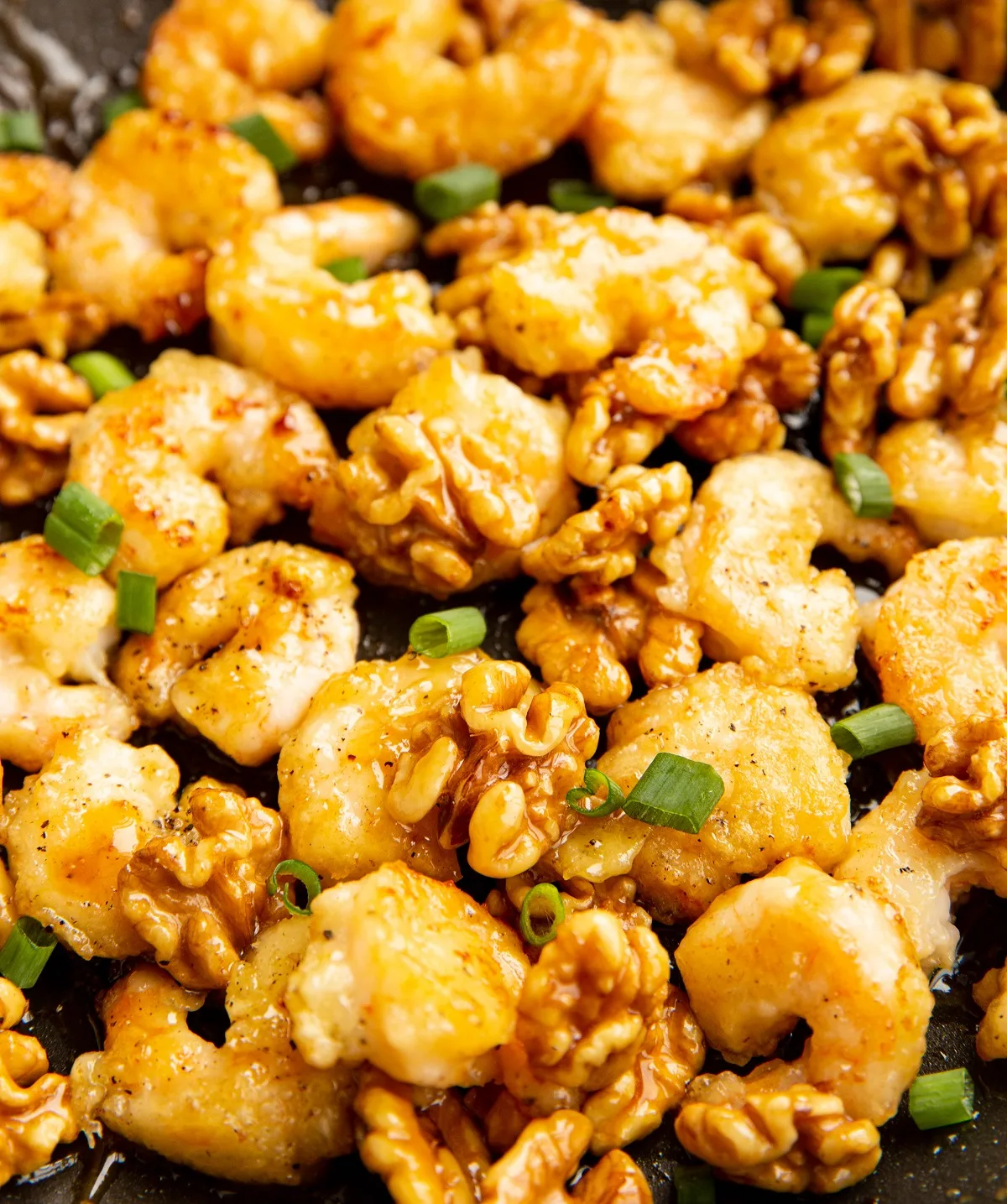 Honey walnut shrimp with green onions sprinkled on top in a skillet