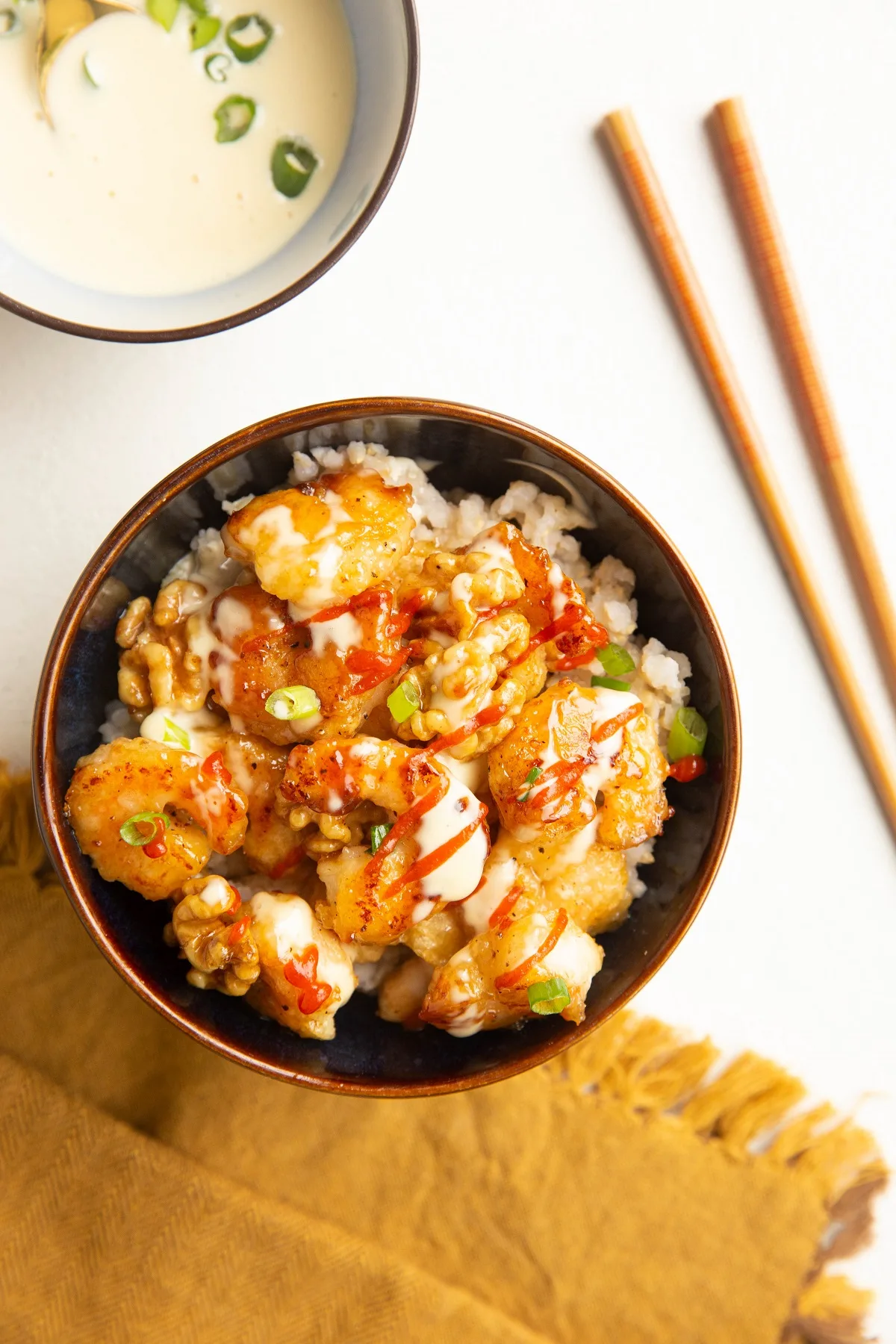 bowl of honey walnut shrimp on top of rice with chop sticks to the side and a bowl of sauce.