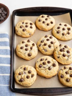 Coconut flour keto cookies on a baking sheet with a blue striped napkin to the side and a wooden bowl of chocolate chips