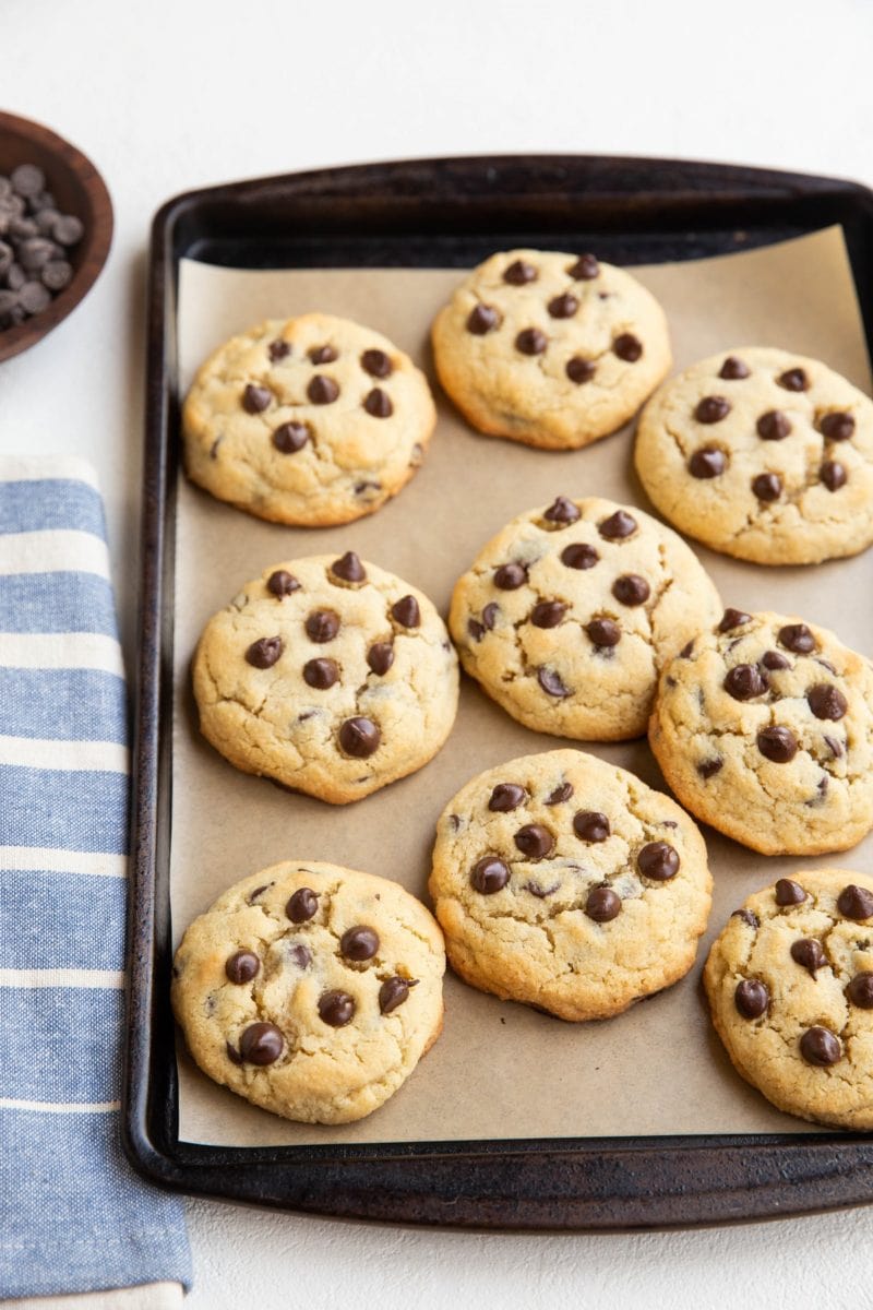 Coconut flour keto cookies on a baking sheet with a blue striped napkin to the side and a wooden bowl of chocolate chips