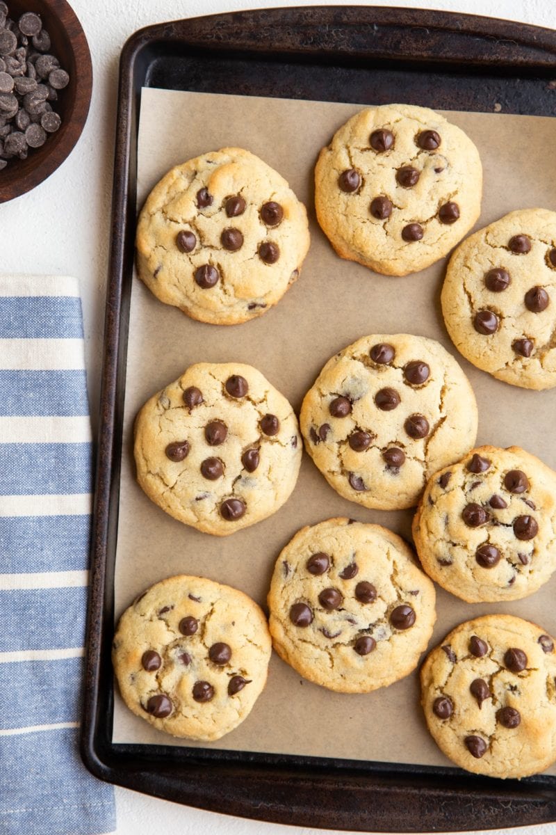 top down image of cookie sheet of chocolate chip cookies with a blue stripe napkin to the side