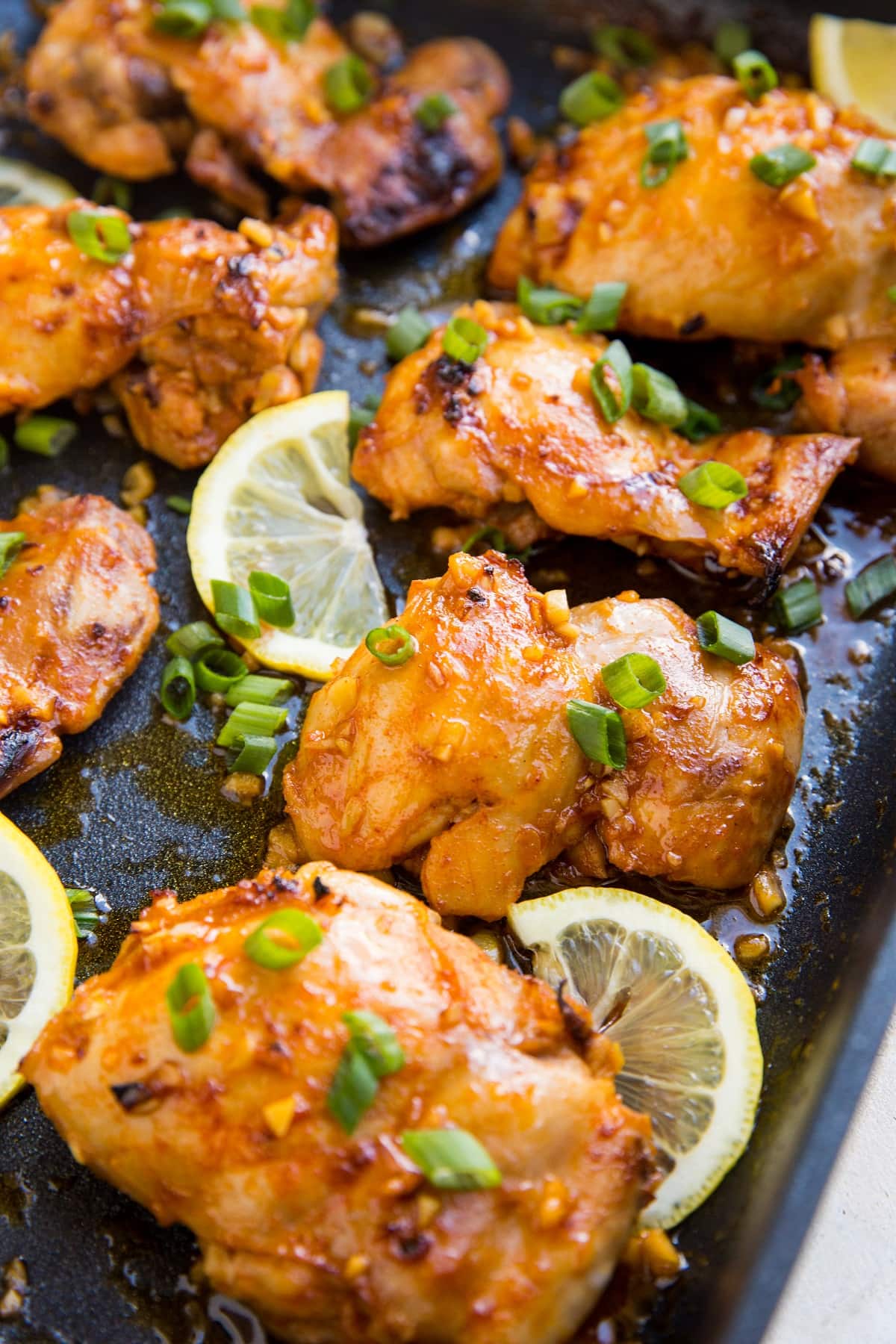 Large black casserole dish with lemon garlic boneless skinless chicken thighs