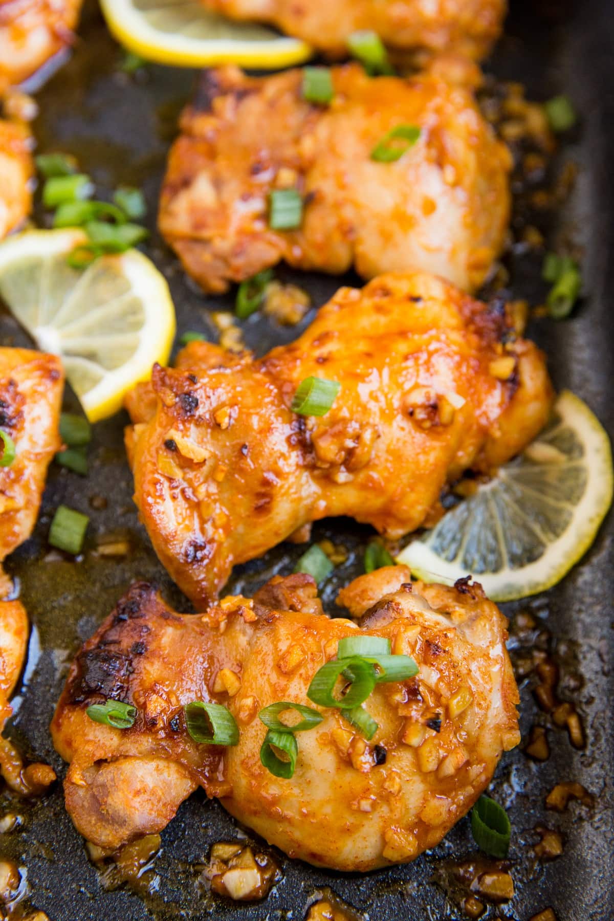 Casserole dish with baked boneless lemon garlic chicken thighs with sliced of lemon and green onion.