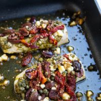 Black roasting pan with Mediterranean Baked Cod inside, fresh out of the oven.