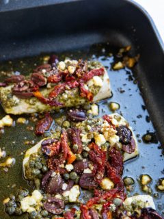 Black roasting pan with Mediterranean Baked Cod inside, fresh out of the oven.