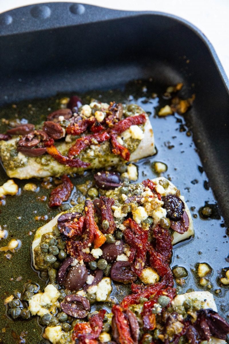 Black roasting pan with Mediterranean Baked Cod inside, fresh out of the oven.