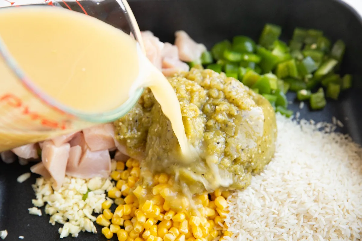 Chicken broth being poured into a casserole dish with casserole ingredients