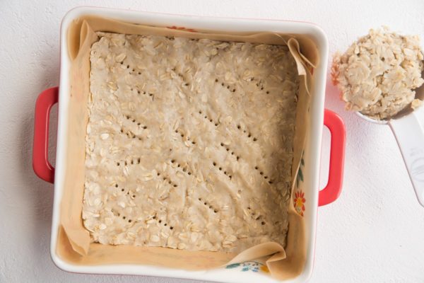 Shortbread crust in a baking dish with a measuring cup of dough off to the side.