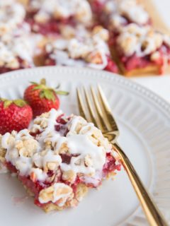 strawberry oatmeal bar on a plate with a gold fork and bars in the background